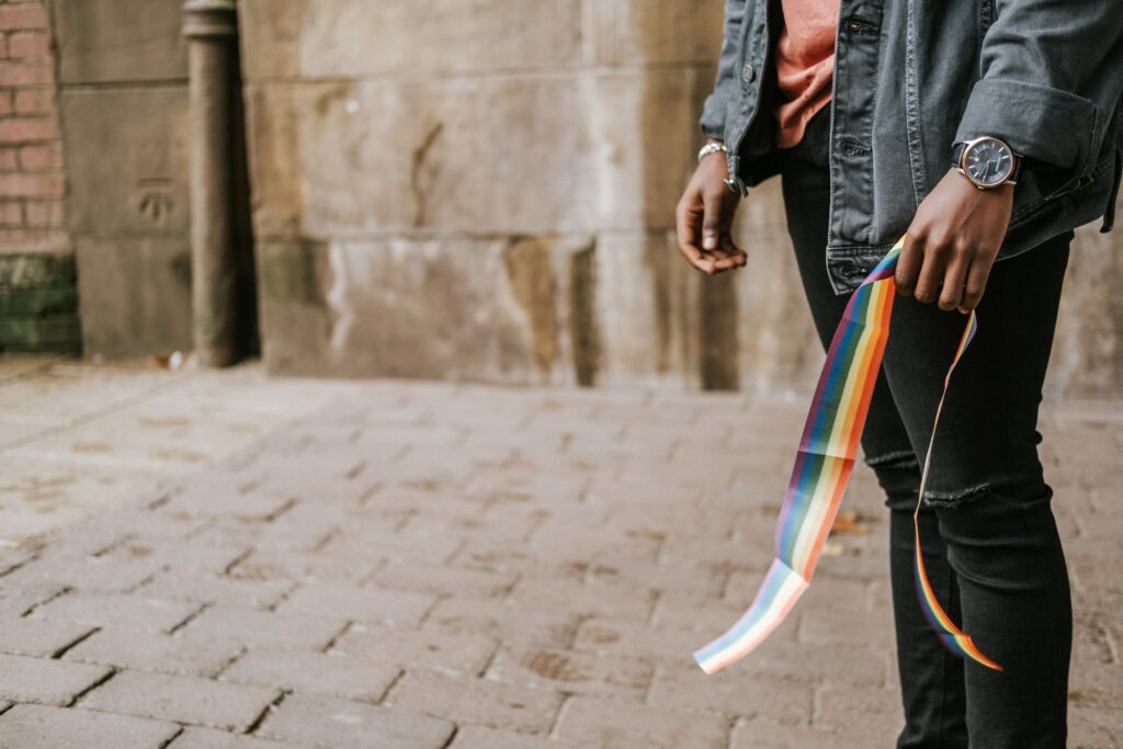 Ein Mensch mit einem Regenbogenband (Pride flag) ist zu sehen.